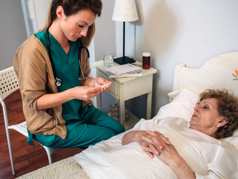 Female doctor taking temperature to senior woman at home